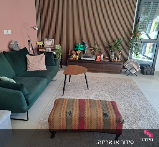 סלון מעוצב ומסודר עם ספה ירוקה, שטיח, קיר חיפוי עץ ומזנון